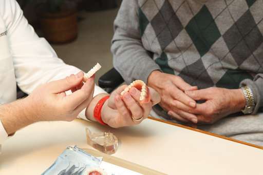 In this Nov. 9, 2016, file photo, Dr. Eric Compton makes a house call with patient Lester Meyer and his wife Rosemary to consult on dental implants in Munster, Ind. Dental implants are increasingly being used to replace missing or failing teeth instead of dentures or bridges, which can be uncomfortable and hasten further deterioration. Experts say dental implants, usually titanium screws inserted into jawbone and capped with a permanent crown, are long-lasting and the best option for most people. (Tony V. Martin/The Times via AP, File)