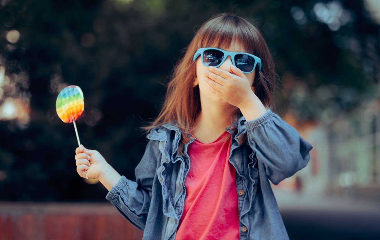 A child holding a sucker and covering her mouth